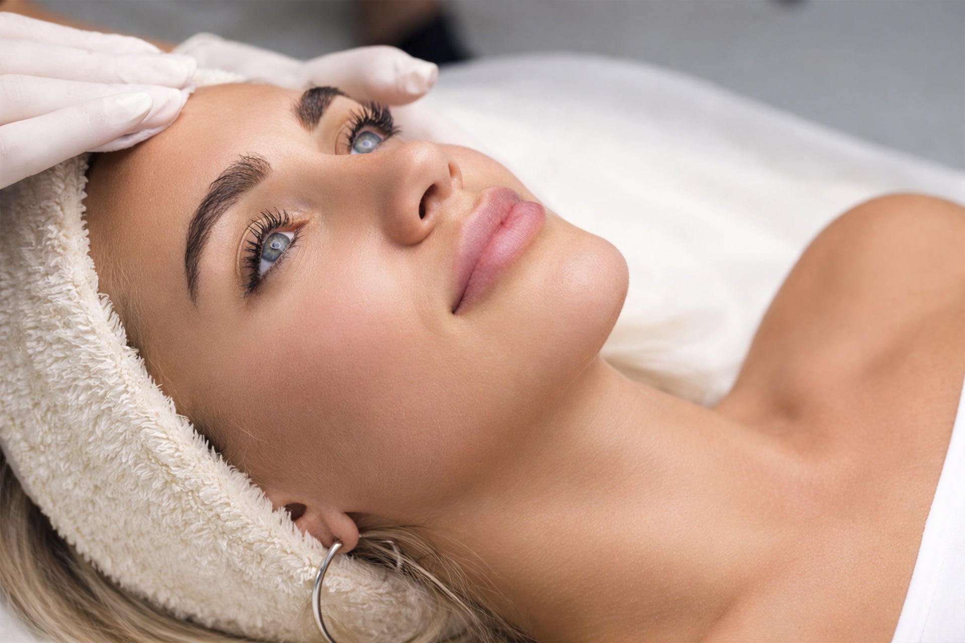 Close-up of a woman receiving a brow lamination treatment, with a technician gently brushing and shaping her brows using a solution, highlighting smooth, fuller, and perfectly groomed eyebrows in a clean, spa-like setting.