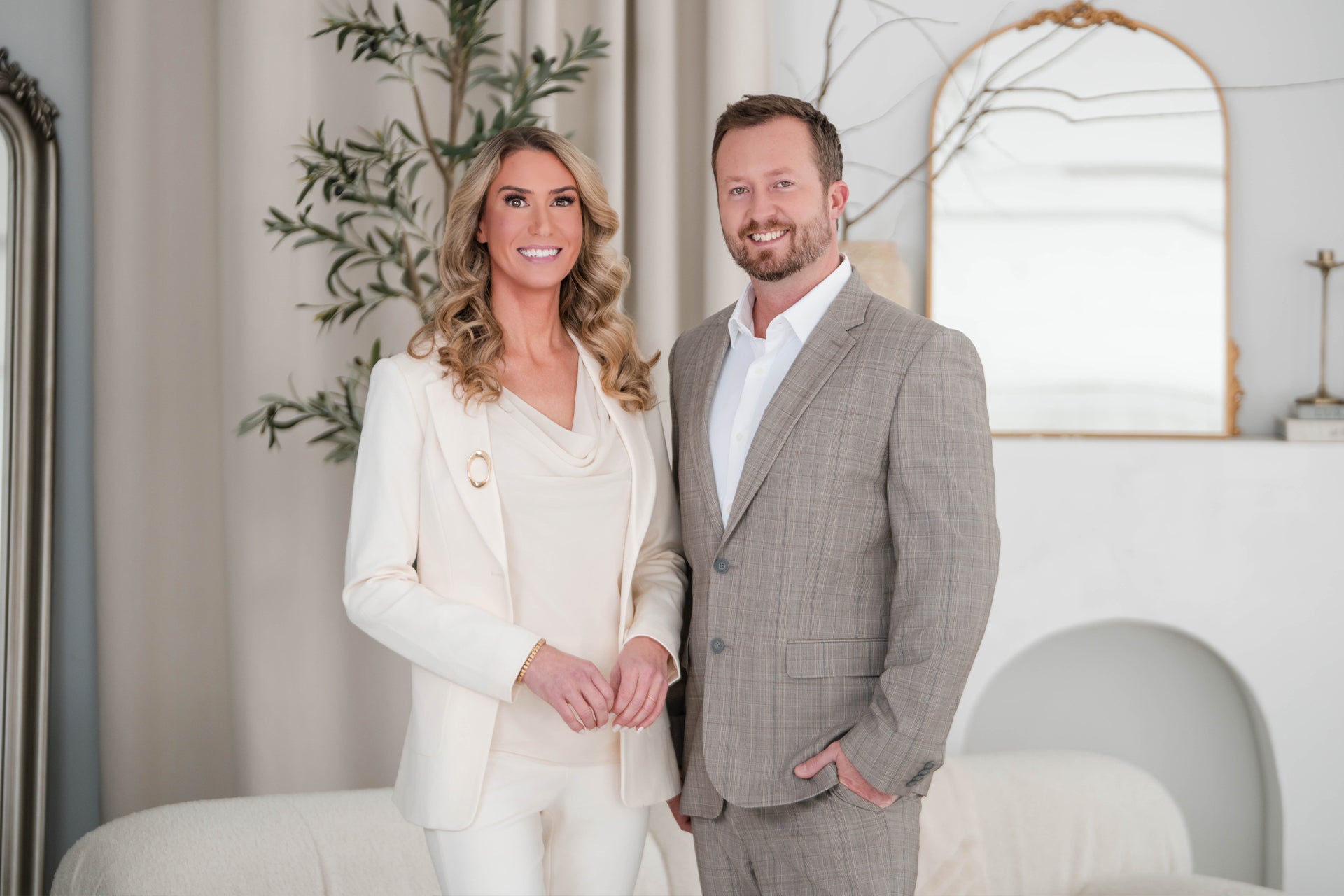 Man and woman in formal attire standing in a stylish room with decor elements.