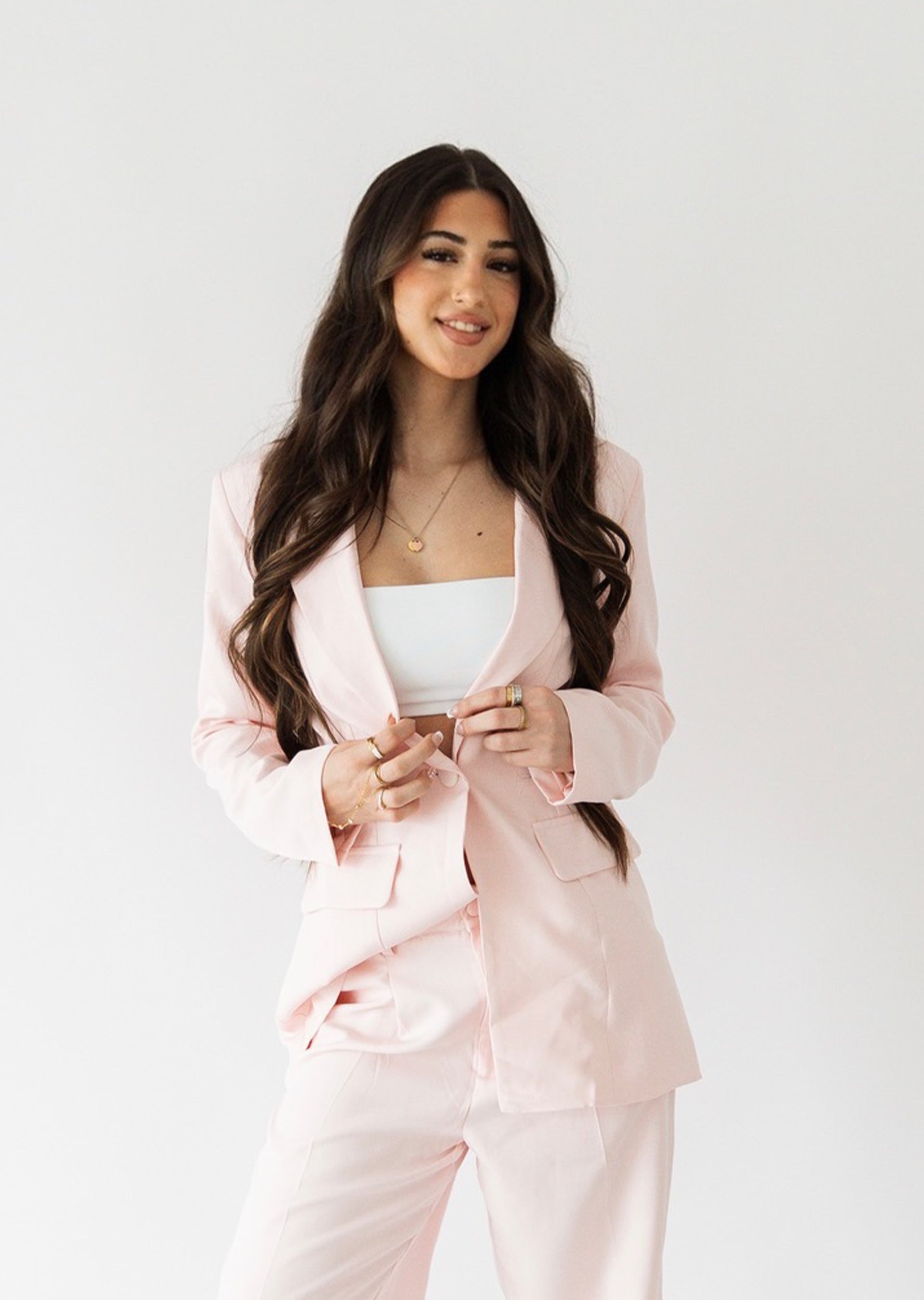Woman wearing a light pink suit with a white top on a plain background